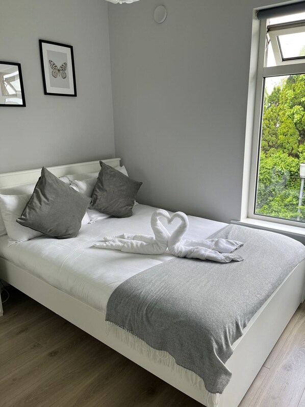 A neatly made bed with a heart-shaped towel arrangement, grey pillows, and a grey throw blanket.