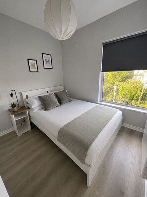 Ein Schlafzimmer mit Bett, Nachttischen, einem Fenster mit Ausblick und Wandbildern.