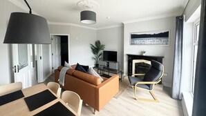A modern living room with a sofa, a dining table, a TV, and a fireplace. - Modern and Spacious No. 6 - sleeps 6 - free parking (Galway)