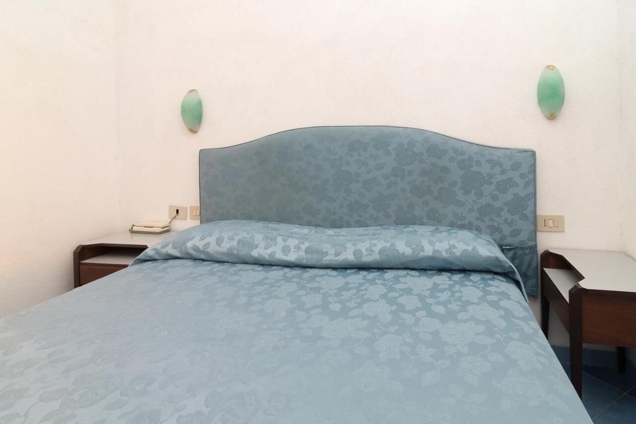 Un dormitorio con una colcha de estampado floral, un cabecero, dos mesitas de noche e iluminación en la pared.