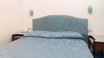 Un dormitorio con una colcha de estampado floral, un cabecero, dos mesitas de noche e iluminación en la pared.