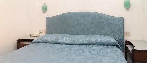 A bedroom with a floral-patterned bedspread, a headboard, two bedside tables, and wall-mounted light fixtures.