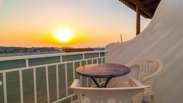 A balcony with a table and chairs, overlooking a cityscape during sunset.
