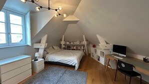 A bedroom with a sloped ceiling, a bed, a desk with a computer, a chair, a bookshelf, and a window. - Like a House. Pleasant Duplex With Air-conditioned Bedrooms, Fully Equipped! (Boulogne-Billancourt)