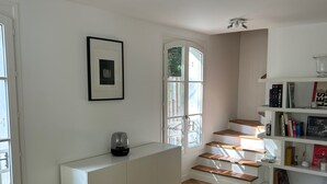 A modern living room with a white console table, a built-in bookshelf, and a staircase with wooden steps. - Like a House. Pleasant Duplex With Air-conditioned Bedrooms, Fully Equipped! (Boulogne-Billancourt)