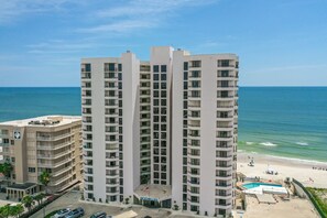 Een hoog hotel met meerdere balkons, een zwembad en uitzicht op het strand.