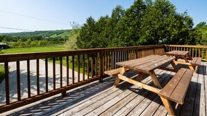 A wooden deck with picnic tables and a railing overlooking a green landscape. - Spacious 8 bdrm Blue Mountain Cottage, Perfect for Large Groups, Private Beach, BBQ, Hot Tub, Sauna (The Blue Mountains)