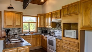 A kitchen with wooden cabinets, a stove, a microwave, and a sink. - Spacious 8 bdrm Blue Mountain Cottage, Perfect for Large Groups, Private Beach, BBQ, Hot Tub, Sauna (The Blue Mountains)