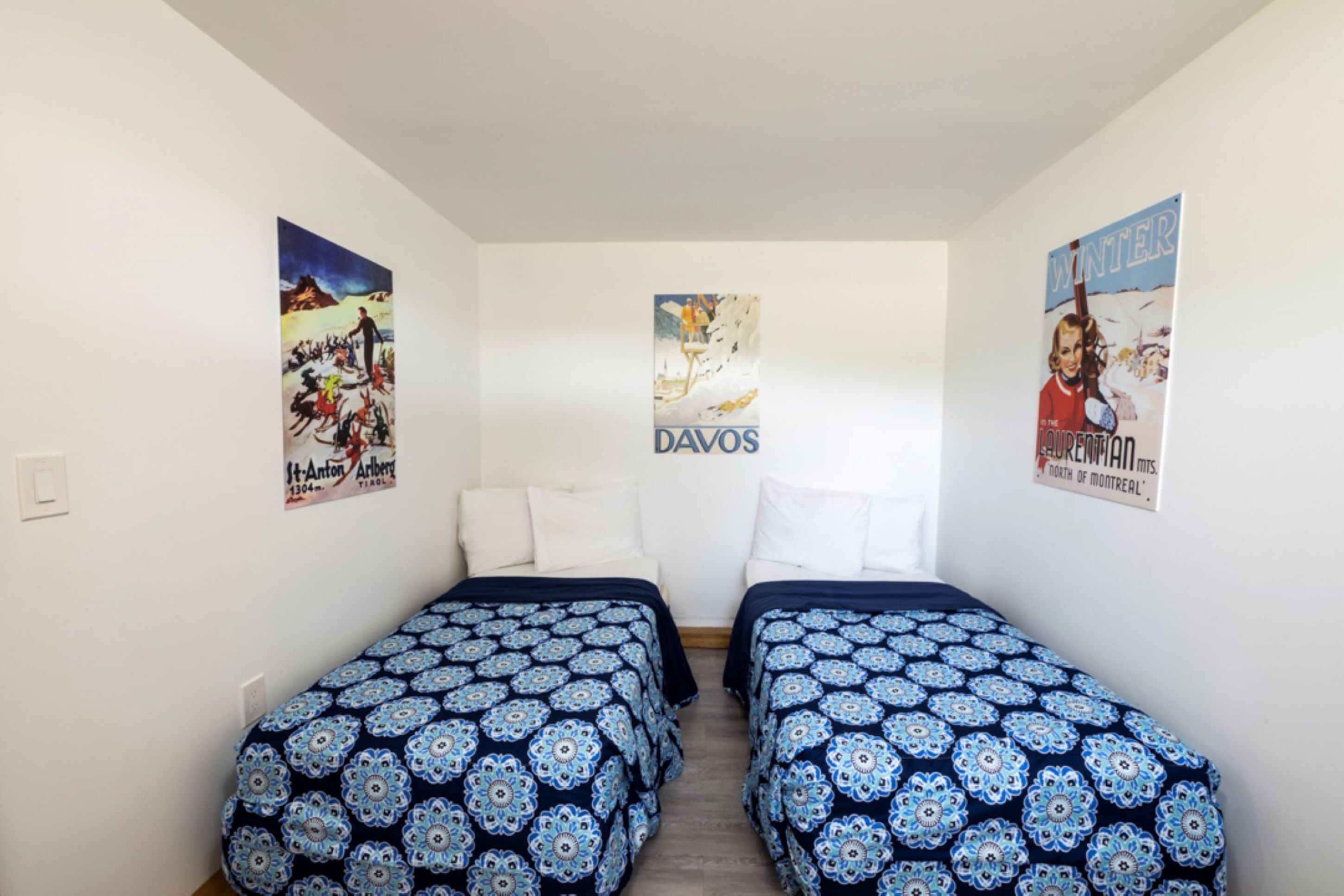 A room with two beds, white walls, and posters on the walls.