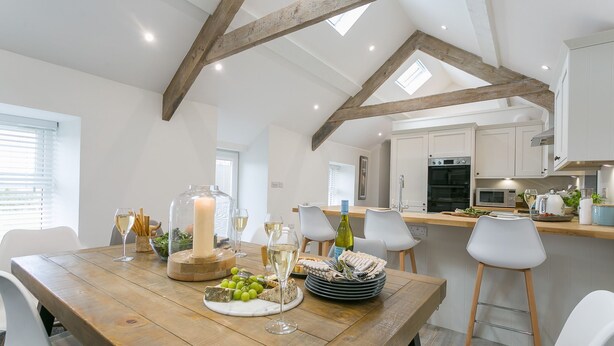 A dining area with a wooden table set for a meal, a large candle centerpiece, and a view of the kitchen in the background. - Ty Capel -  a dog that sleeps 8 guests  in 4 bedrooms (Pentraeth)