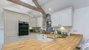 A modern kitchen with white cabinets, a wooden countertop, stainless steel appliances, and a large window. - Ty Capel -  a dog that sleeps 8 guests  in 4 bedrooms (Pentraeth)