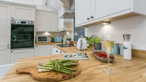 A modern kitchen with white cabinets, a wooden countertop, an oven, a microwave, a kettle, and a glass of white wine. - Ty Capel -  a dog that sleeps 8 guests  in 4 bedrooms (Pentraeth)