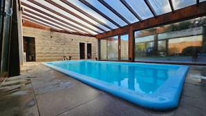 An indoor swimming pool with a glass ceiling, stone walls, and a view through large windows. - COMPLEJO RAICES PATAGONICAS DEPARTAMENTO 3 PERSONAS (Dina Huapi)