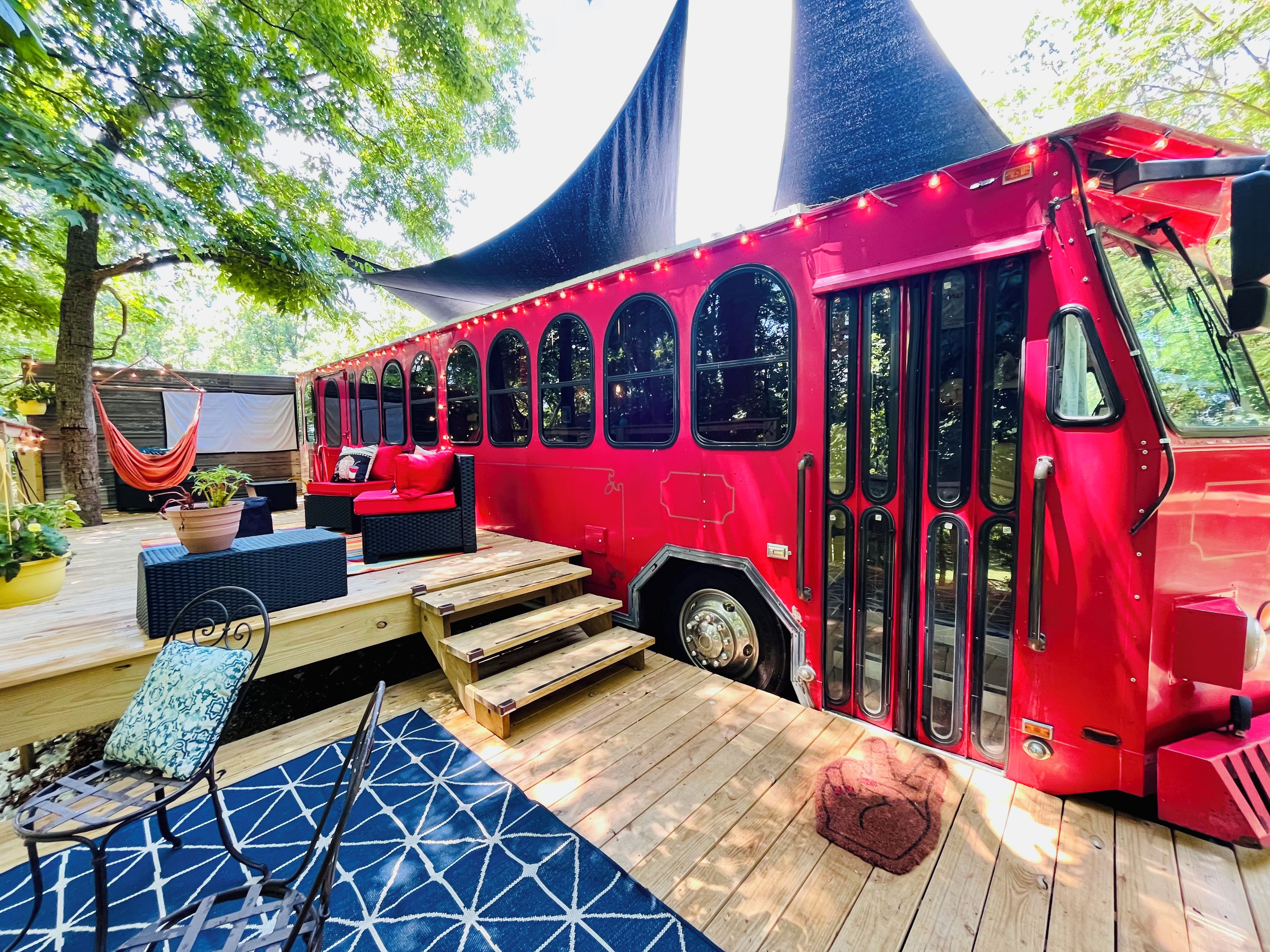 Un autobus rouge transformé en véhicule immobile, doté d’une terrasse, de sièges et d’un hamac.
