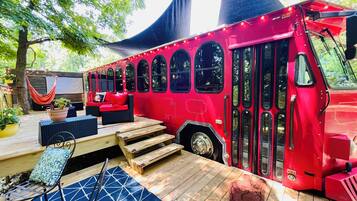 Un autobus rouge transformé en véhicule immobile, doté d’une terrasse, de sièges et d’un hamac.