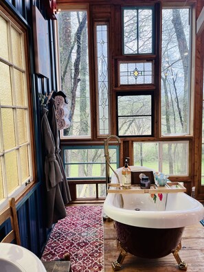 A bathroom with a freestanding bathtub, a wooden floor, and large windows offering a view of trees.