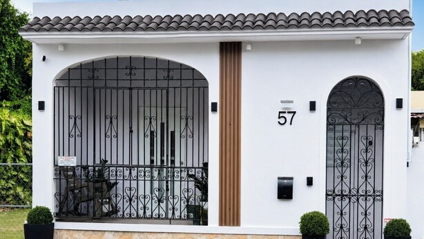 Una casa moderna con un amplio ventanal de arco, el número 57 en la pared y una entrada con reja.