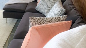 Modulaarinen sohva, jossa on useita tyynyjä, lattiavalaisin ja näkymä luonnonmaisemaan suurten ikkunoiden kautta.