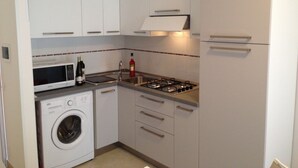 Una cocina compacta con armarios blancos, microondas, cocina a gas y lavadora.