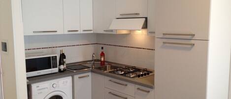 A compact kitchen with white cabinets, a microwave, a gas stove, and a washing machine.