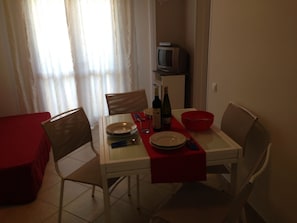 Un coin repas avec une table dressée pour deux personnes, des chaises, un téléviseur et un chemin de table rouge.