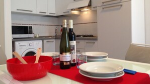 Una cocina moderna con armarios blancos, un mantel rojo, dos botellas de vino y un bol rojo con utensilios de madera.