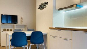 Une cuisine moderne avec des meubles blancs, une cuisinière encastrée et un coin repas agrémenté de deux chaises bleues.