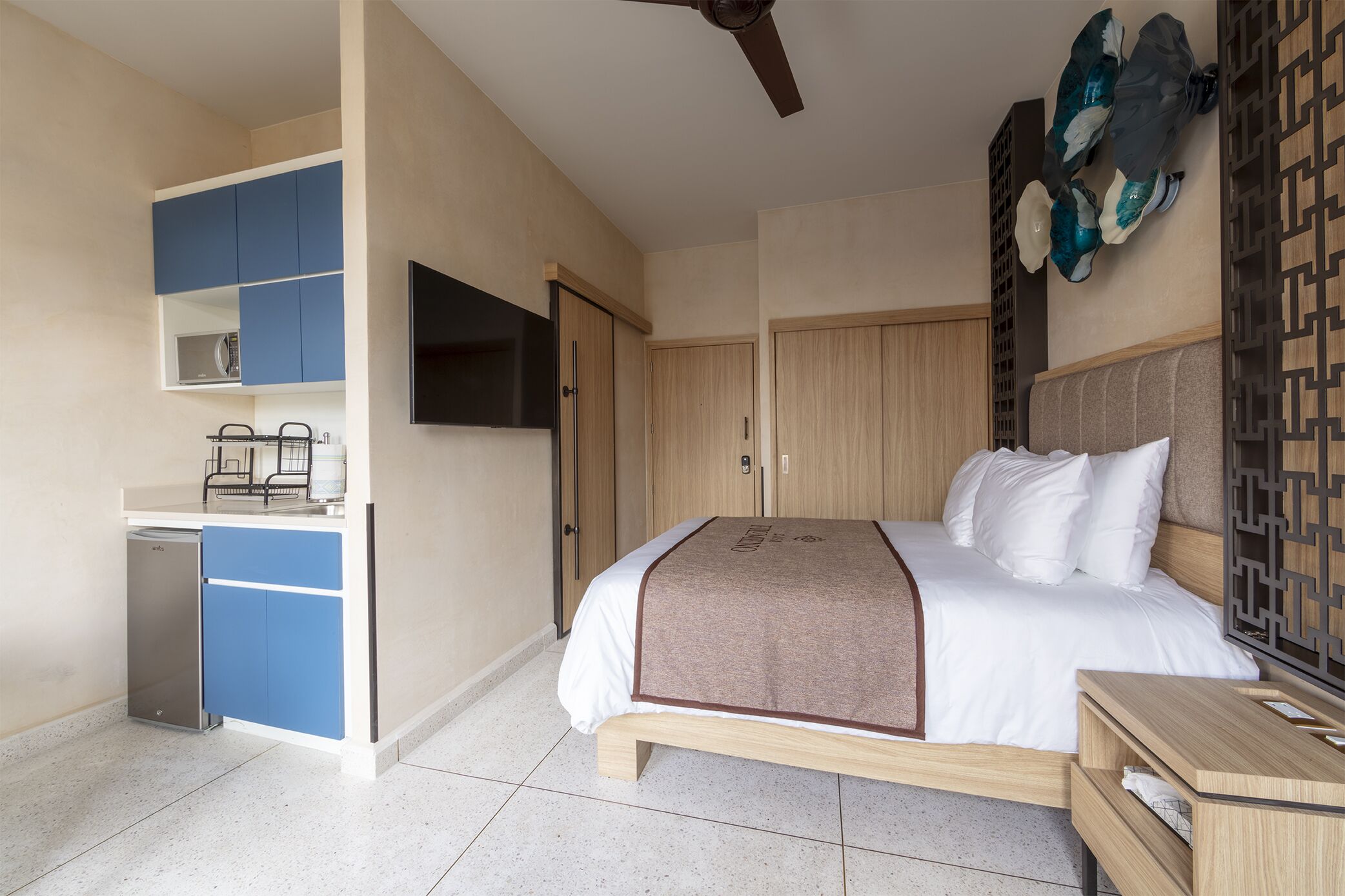 Un dormitorio moderno con cama, televisor, armario y una pequeña kitchenette.