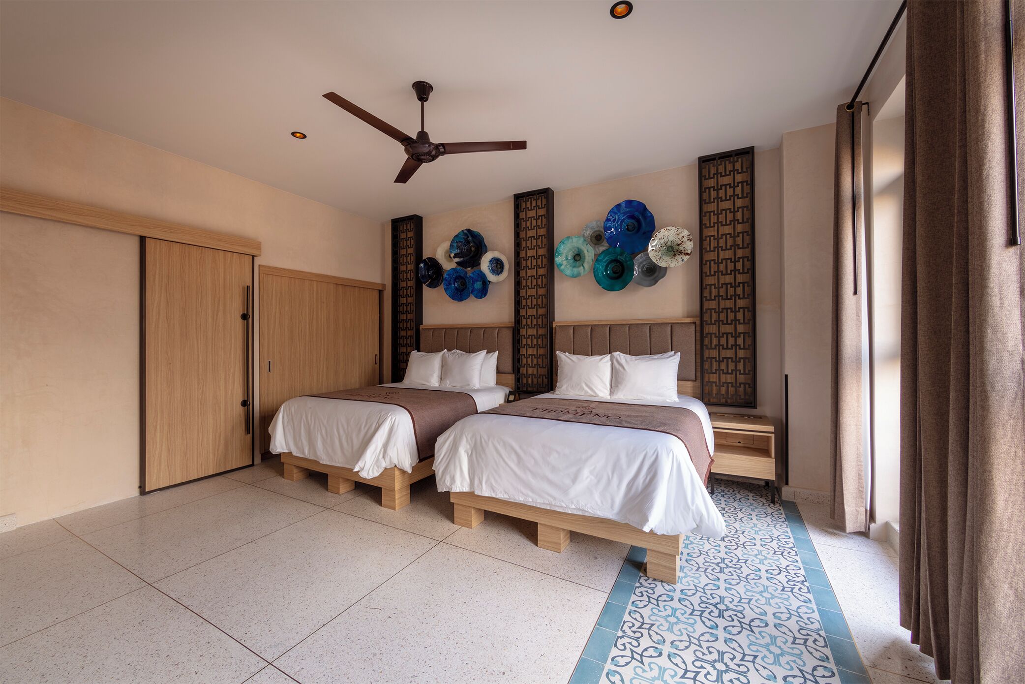 A hotel room with two beds, a ceiling fan, decorative wall art, and a patterned floor.