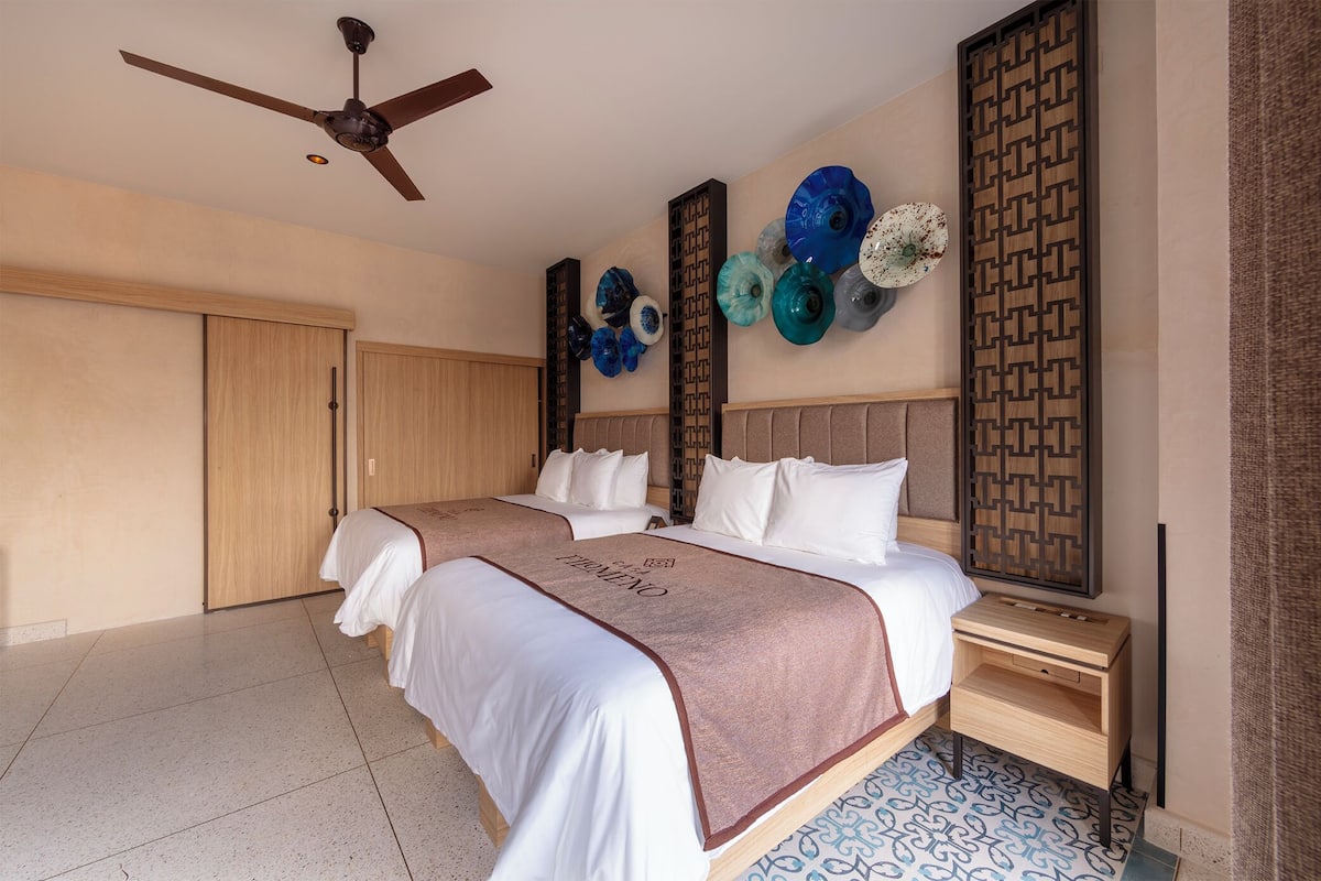 A hotel room with two beds, a ceiling fan, decorative wall art, and a wooden nightstand.