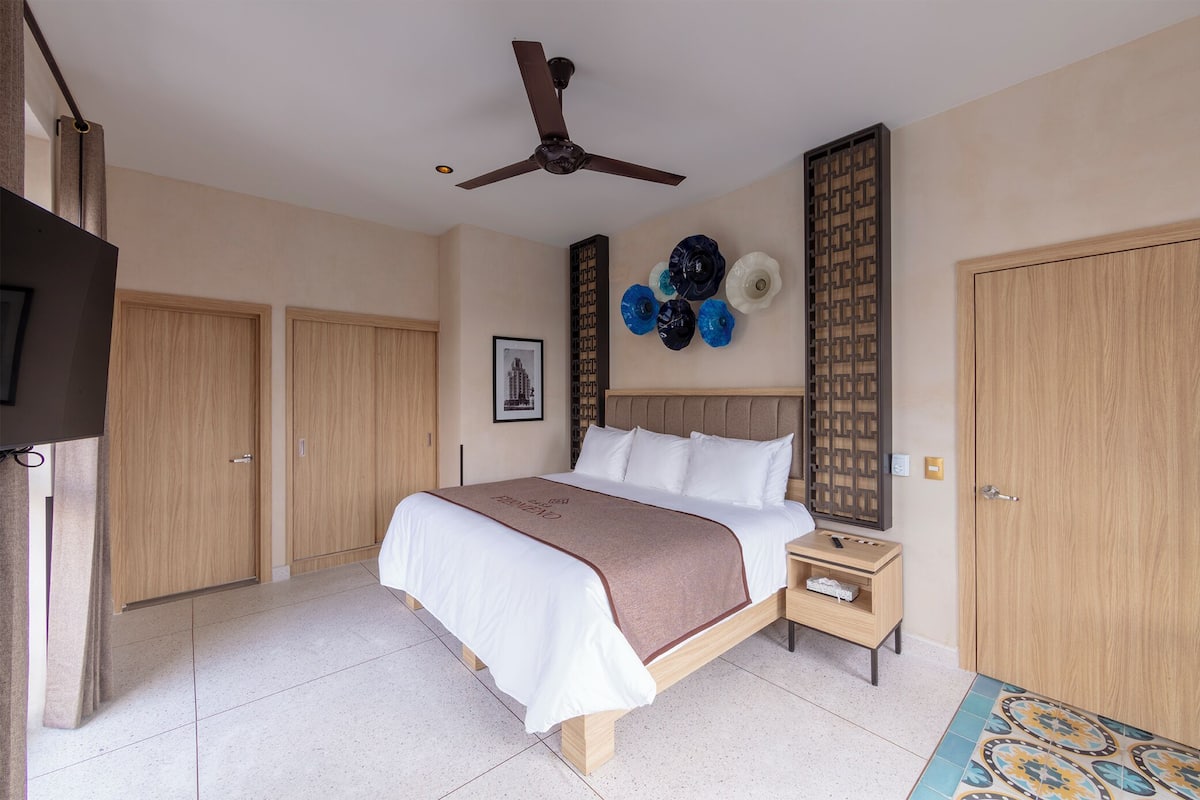 A hotel room with a bed, a nightstand, a ceiling fan, a TV, and wooden doors.