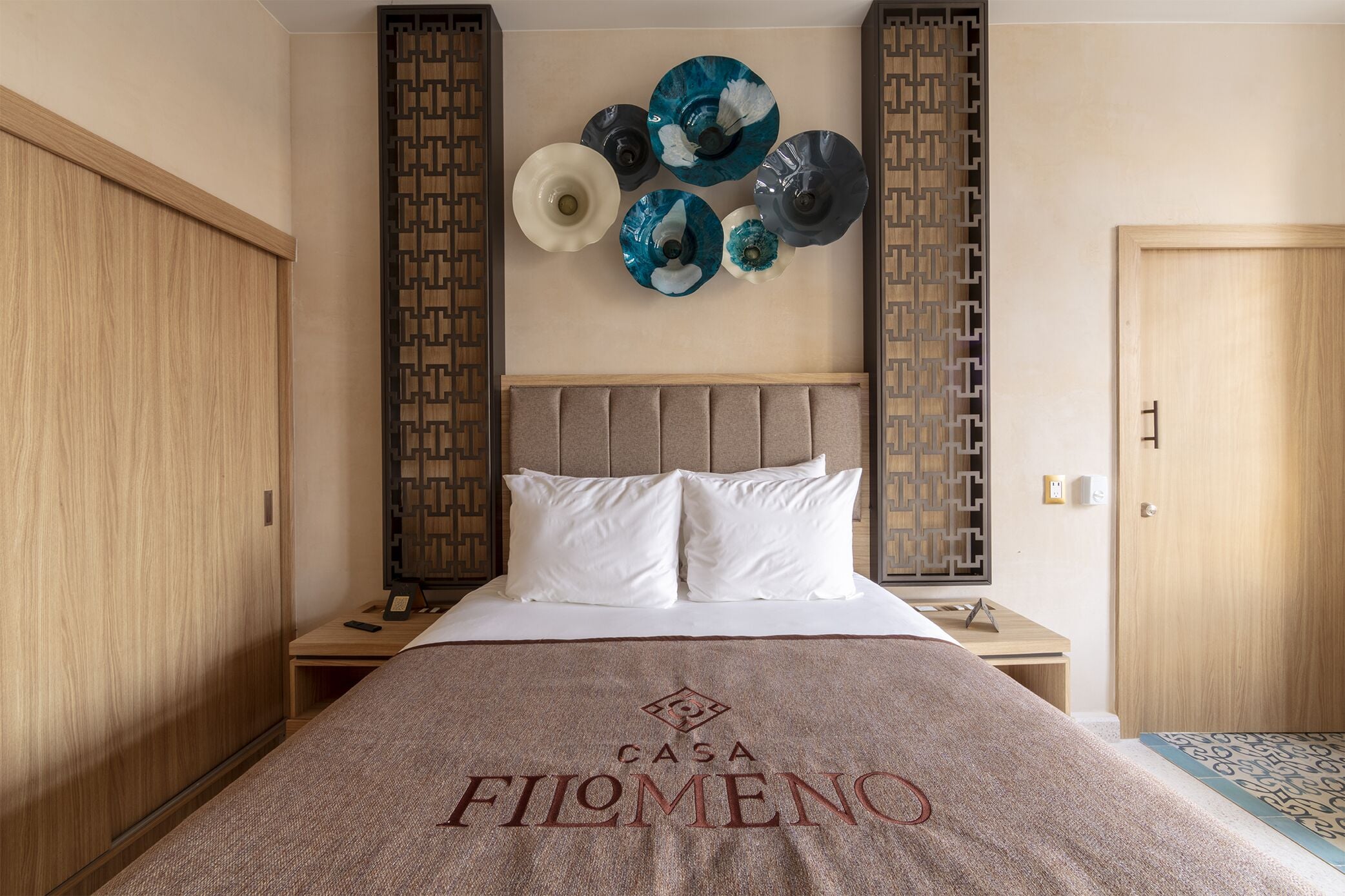 A hotel room with a bed, a nightstand, a wooden wardrobe, and a decorative wall panel.