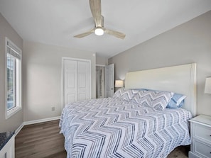 A bedroom with a bed, a ceiling fan, a nightstand, and a window.