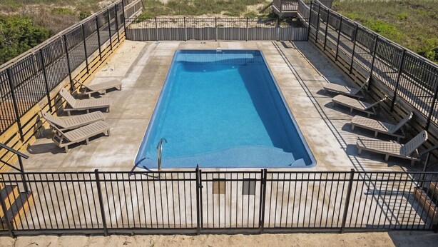 Une piscine rectangulaire entourée d’une terrasse et dotée de chaises longues, offrant une vue sur une plage et l’océan.