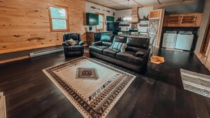 A cozy living room with a dark wood floor, a black leather sofa, and a patterned rug. - Rustic Oak Cabin - dogs welcome - Hocking hills (Logan)
