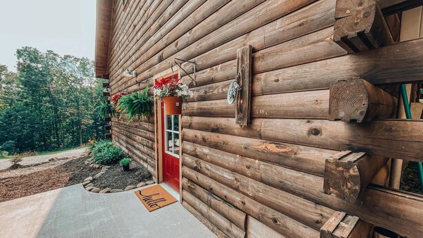 A log cabin with a red door, a welcome mat, and hanging flower baskets. - Rustic Oak Cabin - dogs welcome - Hocking hills (Logan)