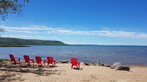 A beach with red chairs facing a calm lake, surrounded by rocks and trees. - Spacious 8 bdrm Cottage with Private Beach Access, BBQ, Hot Tub, Sauna, Pet friendly (The Blue Mountains)