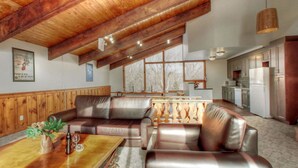 A spacious living area with a wooden ceiling, leather sofas, a wooden coffee table, and a kitchen in the background. - Spacious 8 bdrm Cottage with Private Beach Access, BBQ, Hot Tub, Sauna, Pet friendly (The Blue Mountains)