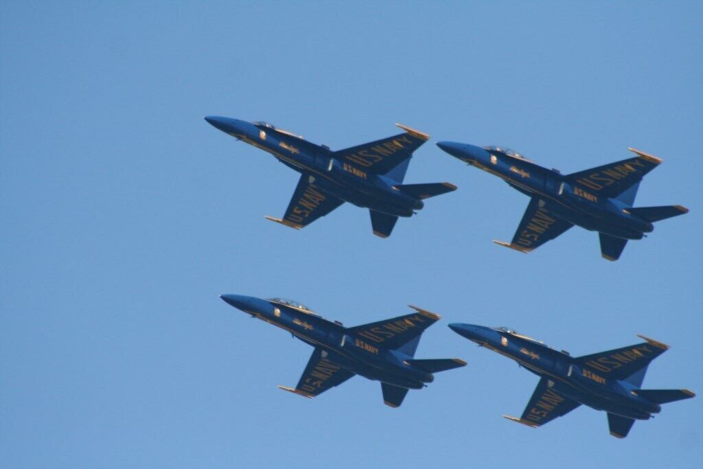Four US Navy aircraft flying in formation against a clear blue sky.