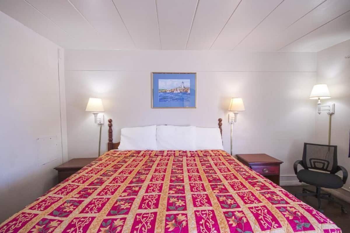 A hotel room with a large bed, two bedside lamps, a desk, and a chair.