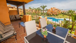 Un balcon avec une table, des chaises et une vue sur une piscine et les bâtiments environnants.