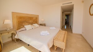 Une chambre avec un grand lit, des tables de chevet, un banc et un miroir au mur.