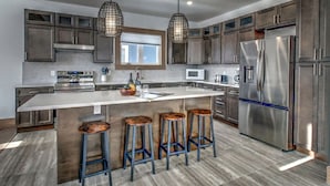 A modern kitchen with a large island, stainless steel appliances, and bar stools. - Brand New 7 bdrm Luxury Cottage with Private Beach Access, BBQ,7.5 baths, Hot Tub, Ping Pong Table (The Blue Mountains)