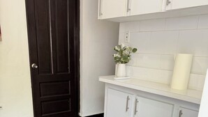 Une cuisine avec des meubles blancs, une porte sombre et une petite plante en pot posée sur le comptoir.