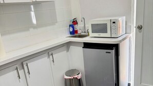 Une cuisine compacte avec des meubles blancs, une poubelle en acier inoxydable, un four à micro-ondes et un évier.