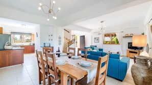 Een ruime woonkamer met een eettafel voor vier personen, een blauwe bank en een keuken op de achtergrond.
