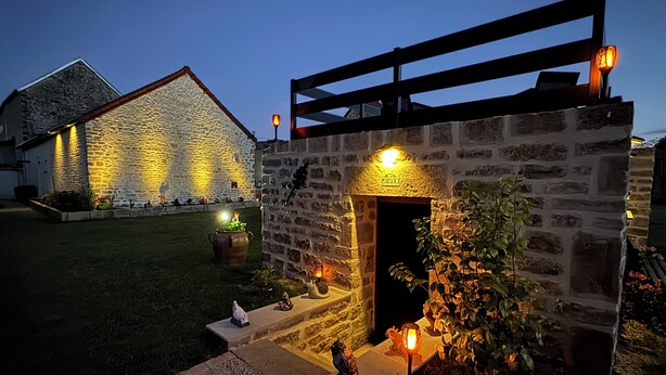 Un bâtiment en pierre avec une entrée illuminée et une pergola en bois au-dessus.