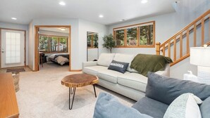 A spacious living room with a light-colored sofa, a round wooden coffee table, and a staircase leading to an upper level. - AC! 2 Kings 2 Twins Condo - Walk to River! Close to downtown and RMNP (Estes Park)