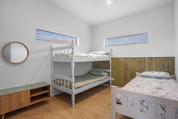 A bunk bed room with a wooden headboard, a small wooden cabinet, and a round mirror on the wall.