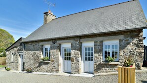 Un bâtiment en pierre, doté d’un toit recouvert de tuiles grises, de portes blanches et de fenêtres à cadres blancs.